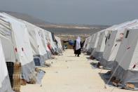 A Syrian woman, who was evacuated from a rebel-held town near Damascus recaptured by gopvernment forces earlier this year, walks between tents at a camp for displaced people at Kafr Lusin in Idlib province close to the Turkish border