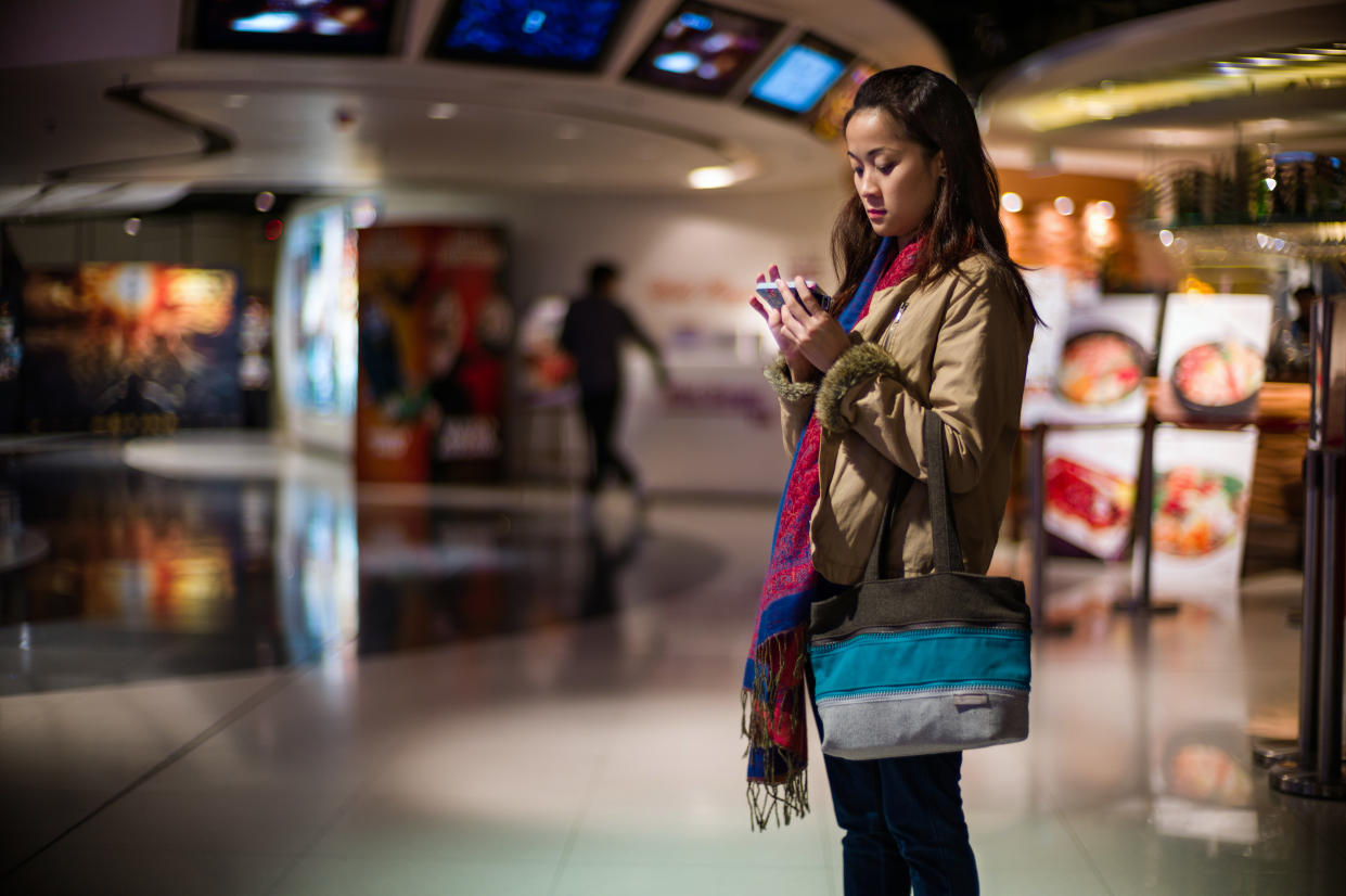 Pretty young lady using a smartphone while waiting to get into the cinema for a movie.