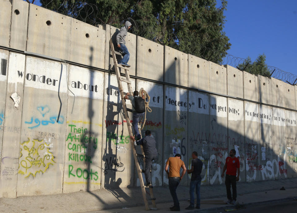 FILE - In this Friday, Aug. 2, 2013, file photo, Palestinians use a ladder to climb over the separation barrier with Israel on their way to pray at the al-Aqsa Mosque in Jerusalem during the Muslim holy month of Ramadan, in Al-Ram, north of Jerusalem. John Kerry’s warning that Israel could become an “apartheid state” if it doesn’t reach a peace deal with the Palestinians has set off an uproar in Israel and angered Israel’s allies in Washington. Kerry was forced to backtrack from his comments, but he voiced an opinion that is frequently heard in Israel itself and tapped into a debate that has become increasingly heated in recent years. (AP Photo/Majdi Mohammed, File)