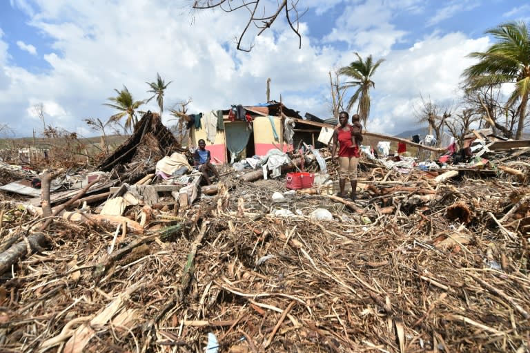 People stand next to their destroyed house in Les Cayes, Haiti, on October 10, 2016, following the passage of Hurricane Matthew