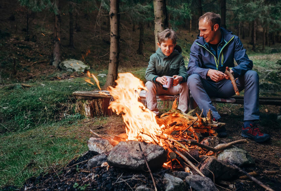 Father with son warm near campfire, drink tea and have conversation (Solovyova / Getty Images)