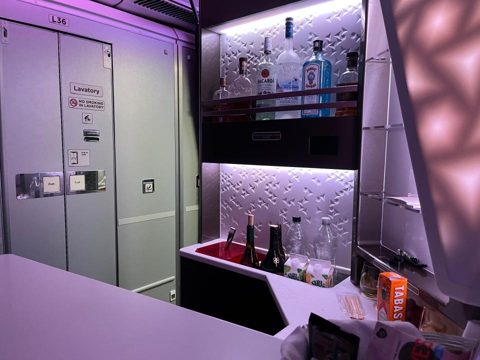 Airplane bar area with shelves stocked with Bacardi, Grey Goose, orange juice, and other mixers