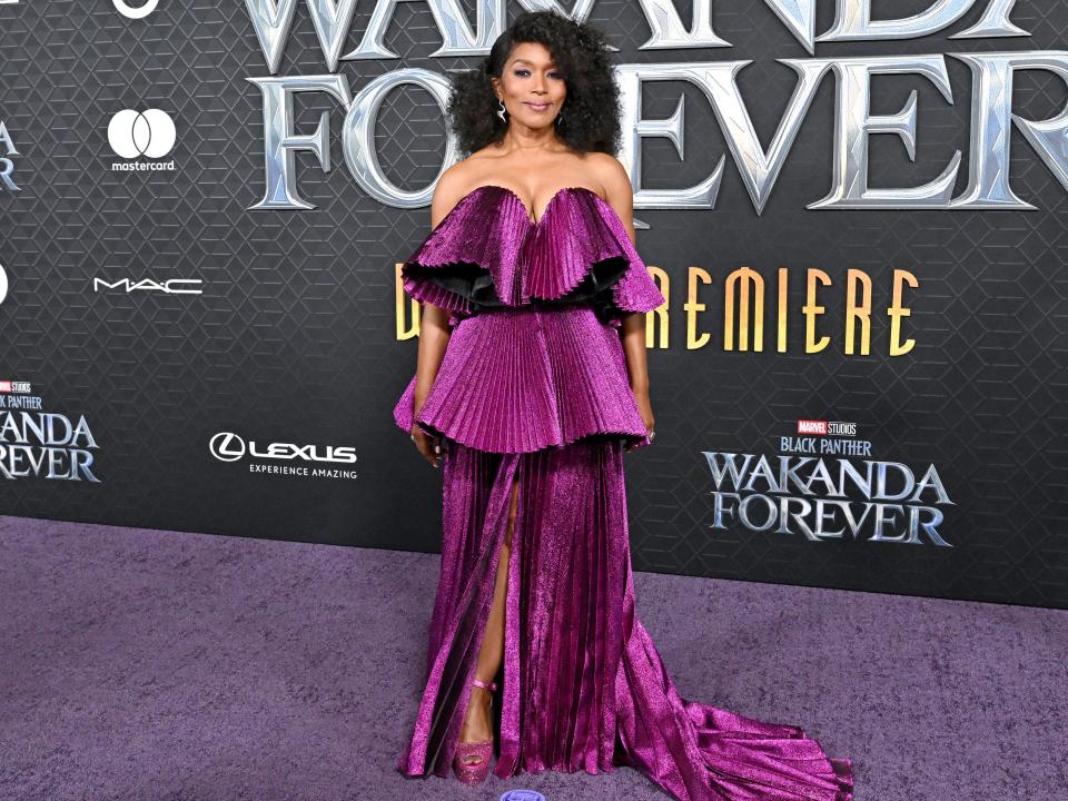 Angela Bassett in purple gown in front of black panther wakanda forever poster