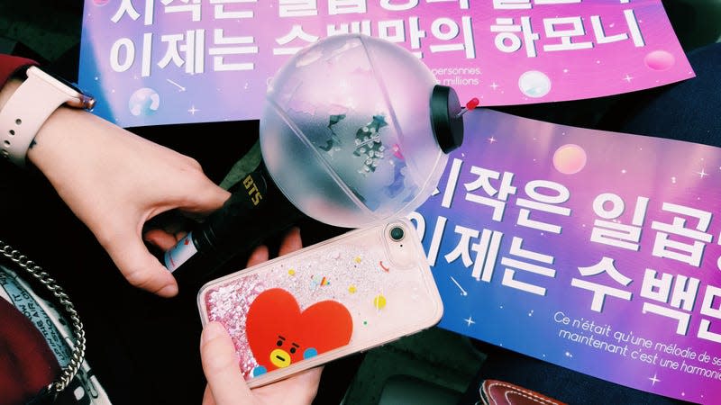 An official BTS ARMY Bomb light stick is shown. It has a black stick for a handle and a clear sphere on top.