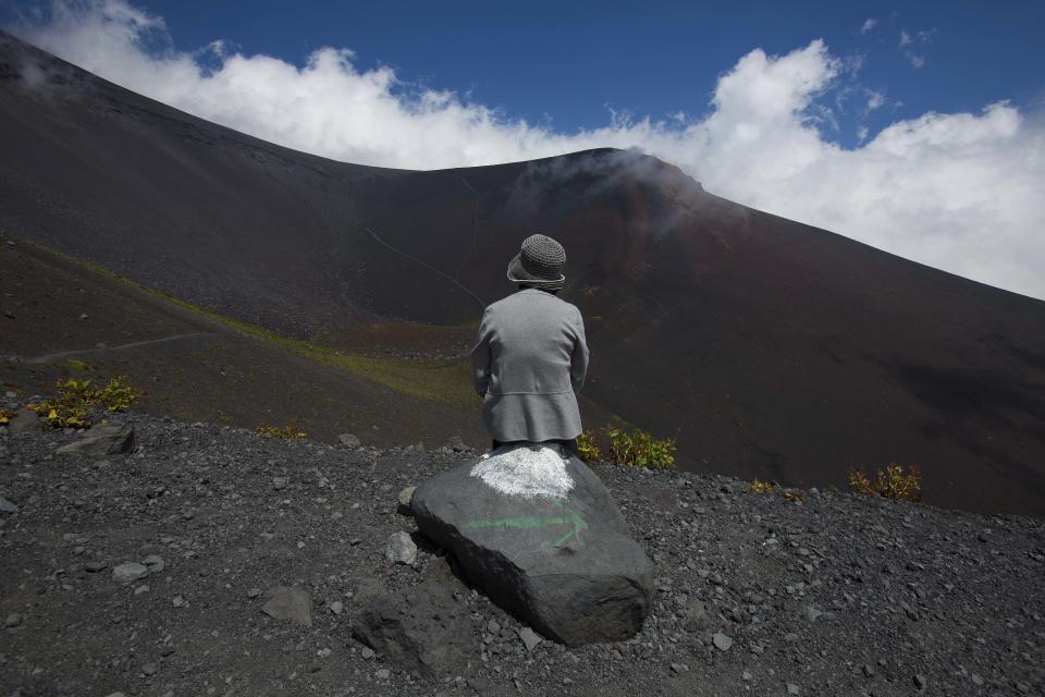 In this Thursday, Aug. 29, 2013 photo, a Japanese woman sits on a rock overlooking a crater on Mount Fuji in Japan. The Japanese cheered the recent recognition of Mount Fuji as a UNESCO World heritage site, though many worry that the status may worsen the damage to the environment from the tens of thousands who visit the peak each year. (AP Photo/David Guttenfelder)