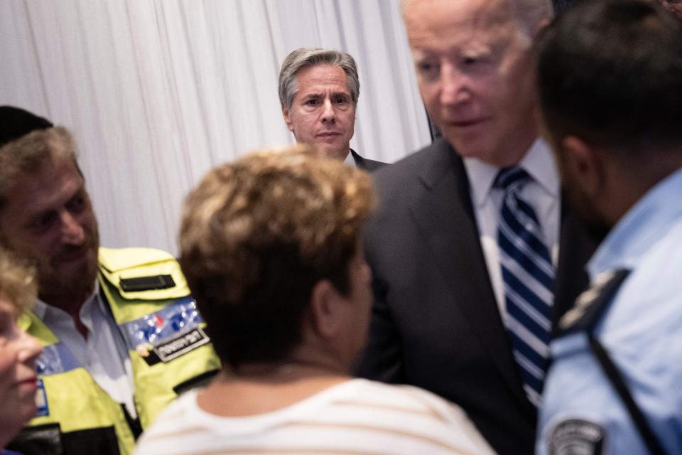 A photo of Antony Blinken watching on as President Biden speaks to others.