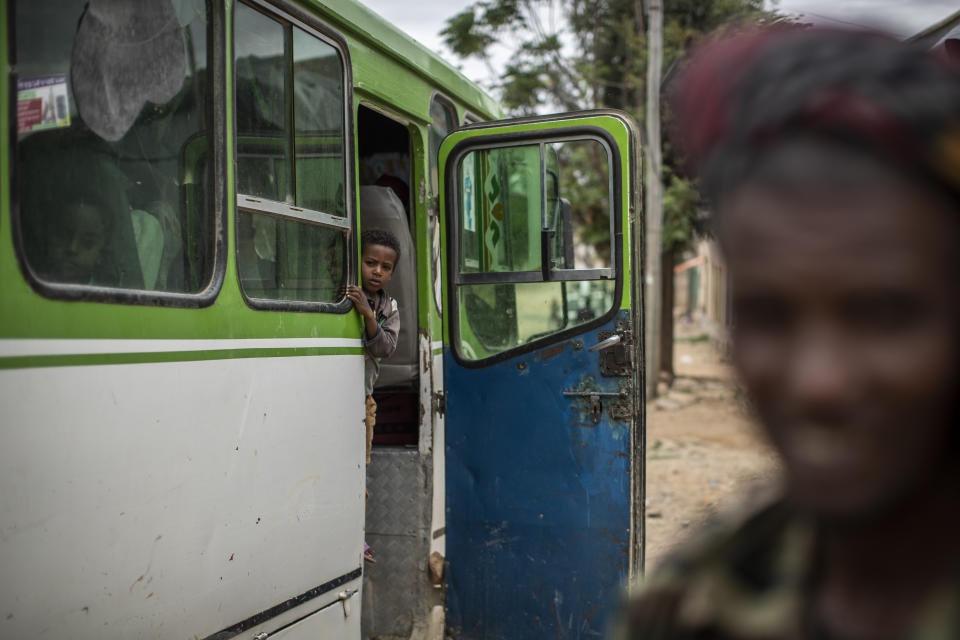 A boy about to depart on a bus looks towards a fighter loyal to the Tigray People's Liberation Front (TPLF), right, in the town of Hawzen, then-controlled by the group, in the Tigray region of northern Ethiopia, on Friday, May 7, 2021. Residents of Hawzen, a town of a few thousand people, said it had seen fighting four times since November. (AP Photo/Ben Curtis)