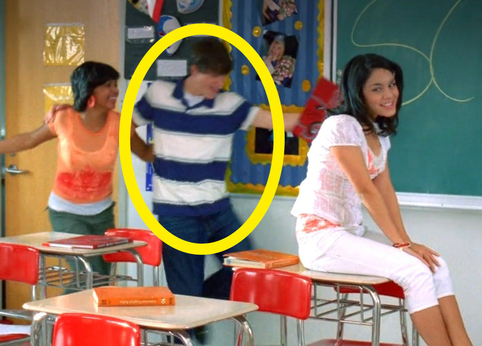 Shane circled while standing between two girls next to a blackboard in a classroom scene