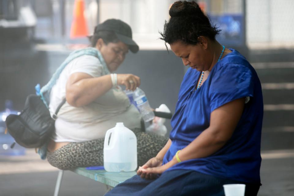 A woman sits under evaporative coolers as temperatures exceed 105 degrees at Andre House who offers services for the homeless in Phoenix on July 12, 2021.