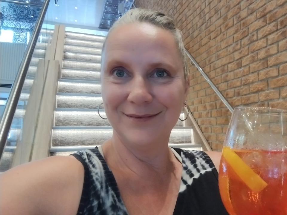 A woman posing for a selfie while standing on a white stairway with an orange drink in her hand.