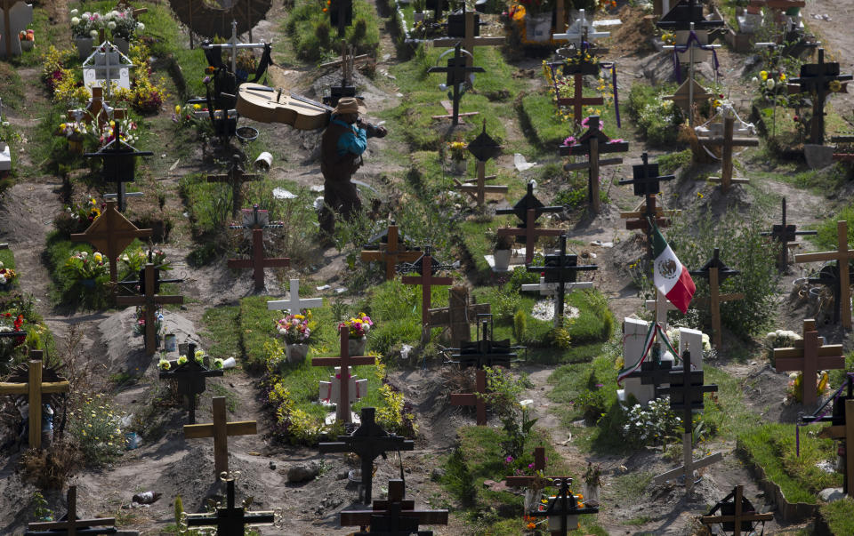 A musician walks through the municipal cemetery Valle de Chalco amid the new coronavirus pandemic, on the outskirts of Mexico City, Tuesday, Oct. 20, 2020. Mexican families traditionally flock to local cemeteries to honor their dead relatives as part of the “Dia de los Muertos,” or Day of the Dead celebrations, but according to authorities the cemeteries will be closed this year to help curb the spread of COVID-19. (AP Photo/Marco Ugarte)