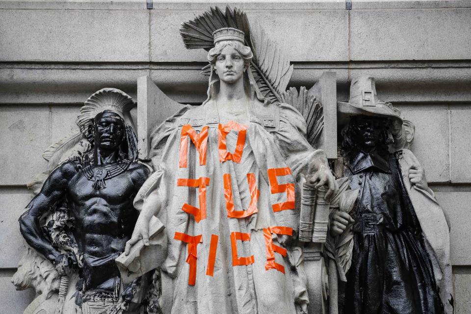 Statues are defaced outside government buildings as protesters gather at an encampment outside City Hall, Tuesday, June 30, 2020, in New York. New York City lawmakers are holding a high-stakes debate on the city budget as activists demand a $1 billion shift from policing to social services and the city grapples with multibillion-dollar losses because of the coronavirus pandemic. (AP Photo/John Minchillo)