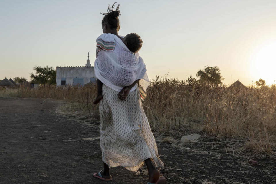 A Tigrayan woman who fled the conflict in Ethiopia's Tigray region, carries her baby to attend Sunday Mass at a church, near Umm Rakouba refugee camp in Qadarif, eastern Sudan, Nov. 29, 2020. (AP Photo/Nariman El-Mofty)