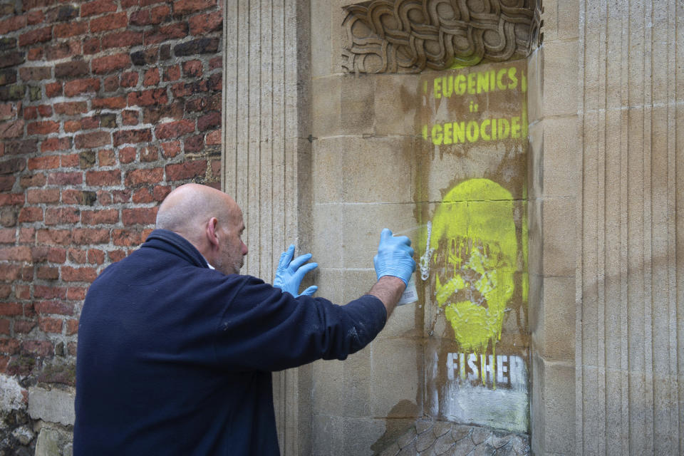 A man tries to remove a spray painted writing "Eugenics is genocide. Fisher must fall" on Ronald Fisher, founder of the Cambridge Eugenics society, by activists on the Gate of Honor, of Cambridge University, in Cambridge, Britain, Friday, June 12, 2020, following Black Lives Matter protests that took place across the UK over the weekend. The protests were ignited by the death of George Floyd, who died after he was restrained by Minneapolis police on May 25. (Aaron Chown/PA via AP)