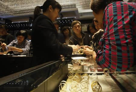 Sales attendant shows gold bracelet to customers leaning over a half-empty display case at a jewellery store in Hong Kong