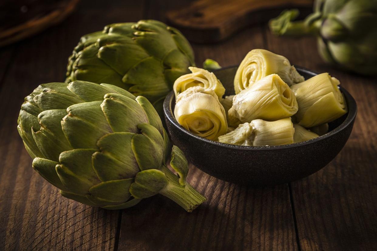 artichoke hearts on a black bowl surrounded by artichokes