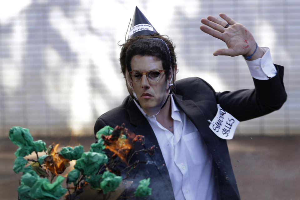 An activist, wearing a mask depicting Environment Minister Ricardo Salles, holds an object representing the Amazon forest on fire, during a protest against the government's environmental policies, marking World Environment Day, in Brasilia, Brazil, Saturday, June 5, 2021. (AP Photo/Eraldo Peres)