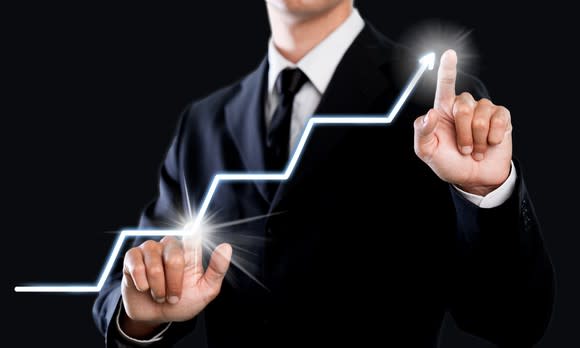 Man in business attire pointing to lighted line chart going up