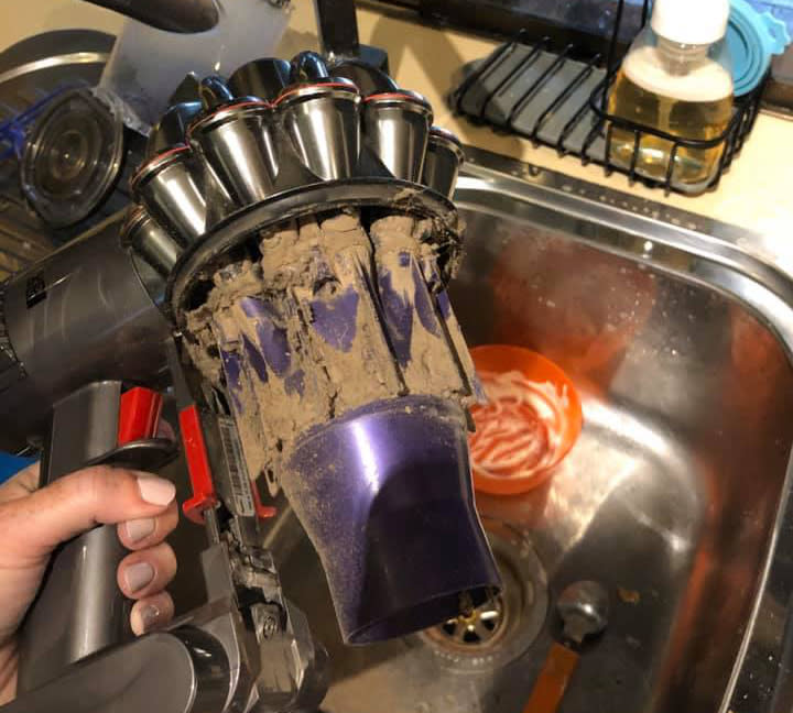 Mum shows photo of inside the Dyson vacuum cleaner, holds machine above sink, purple plastic is covered in thick dust and debris