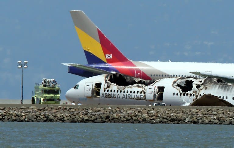 An Asiana Airlines flight enroute to South Korea taxis past the wreckage of flight 214 as it sits on the runway of San Francisco International Airport on July 8, 2013