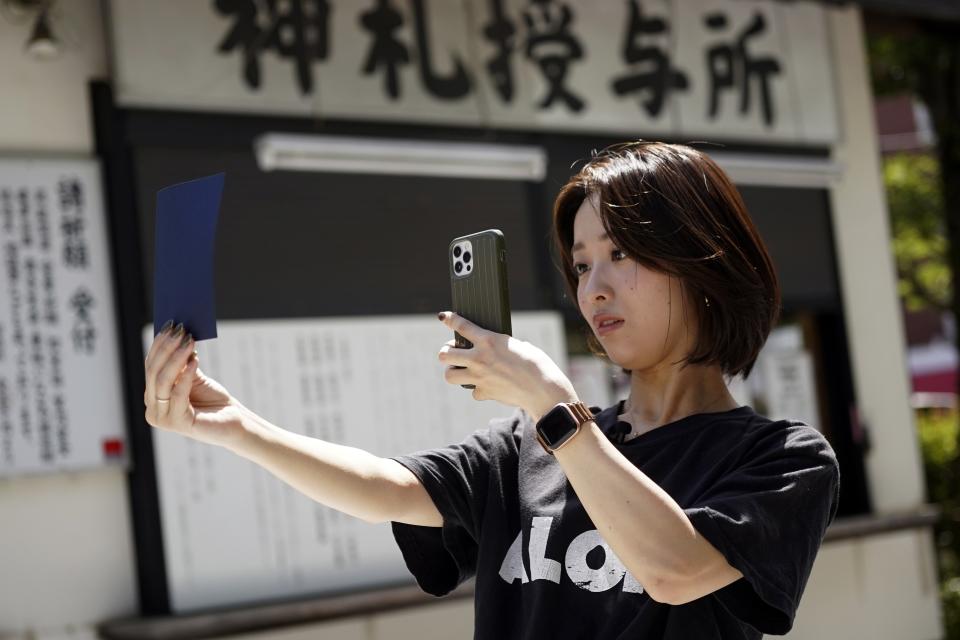 Momo Nomura, a graphic artist and entrepreneur, photographs a newly collected Goshuin, a seal stamp certifying her visit that comes with elegant calligraphy and the season’s drawings, at Sakura Jingu shrine in Tokyo on Aug. 30, 2023. “Because of the Goshuin, shrines have become closer to me, but I don’t consider this a religious activity,” Nomura said. (AP Photo/Eugene Hoshiko)