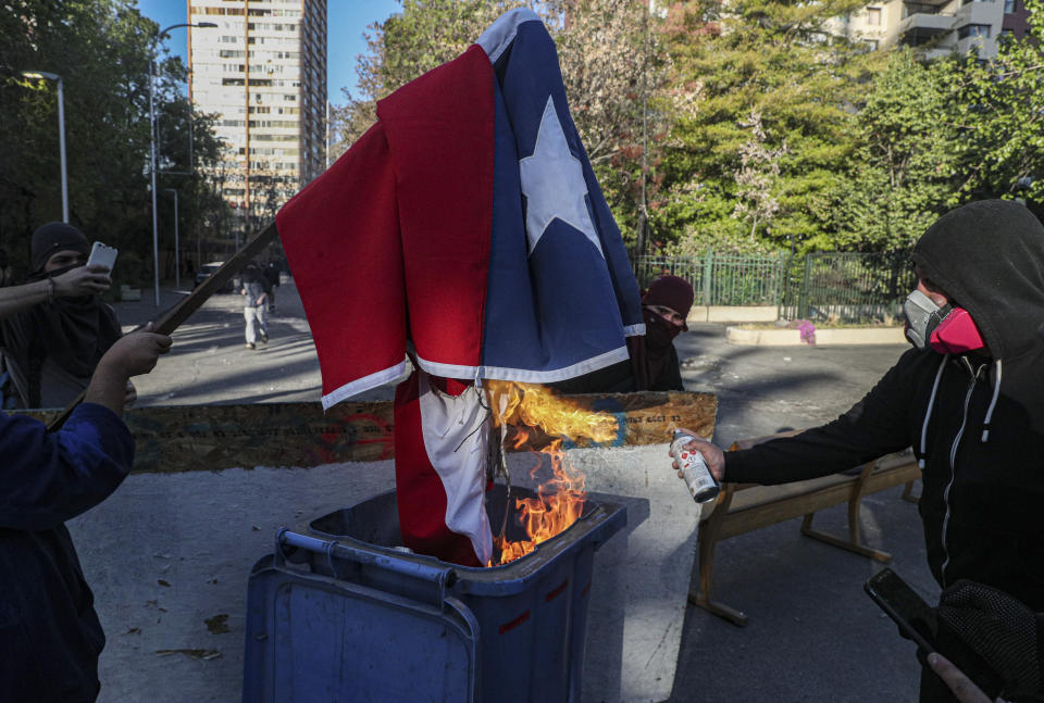 Demonstrators burn a Chilean flag during a protest against police in reaction to a video that appears to show an officer pushing a youth off a bridge the previous day at a protest, in Santiago, Chile, Saturday, Oct. 3, 2020. (AP Photo/Esteban Felix)