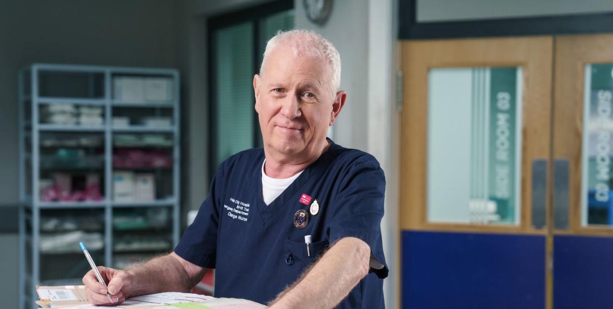 casualty star derek thompson in character as charlie fairhead, writing in a medical report at the nurses' station
