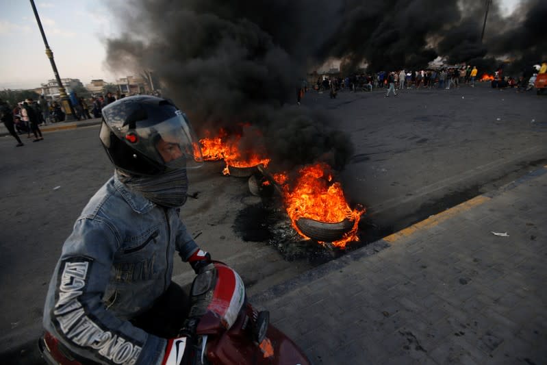 A man rides his motorbike near burning tires during ongoing anti-government protests in Basra