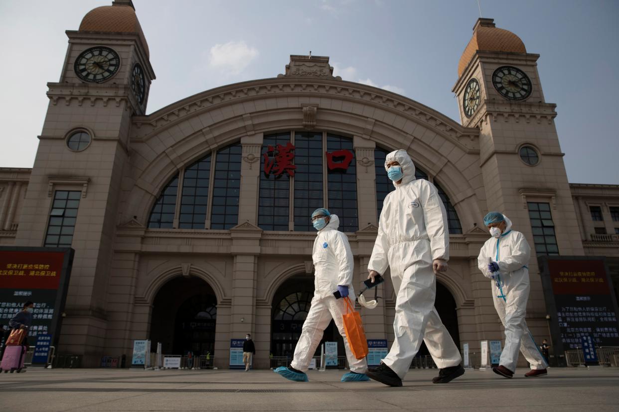 <p>Workers in protective suits walk through central Wuhan</p> (AP)