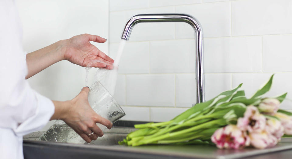 Woman pouring fresh water into a glass vase with tulip on the side