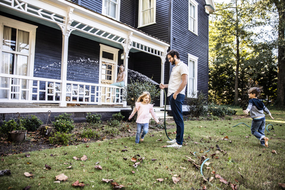 Father watering lawn, children playing in hose