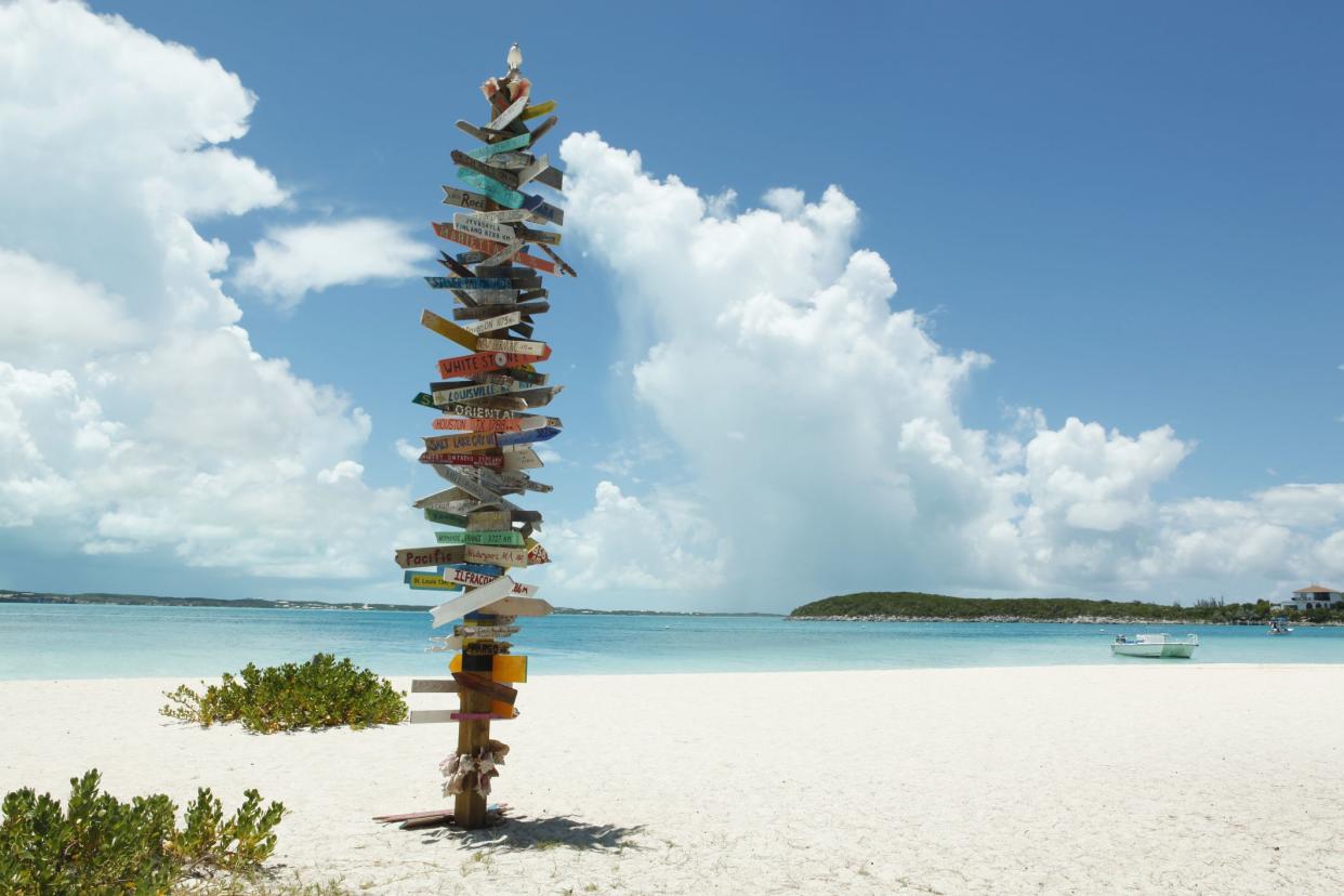 Directional sign with numerous cities on Stocking Island, Bahamas, sunny day on the beach with white sand