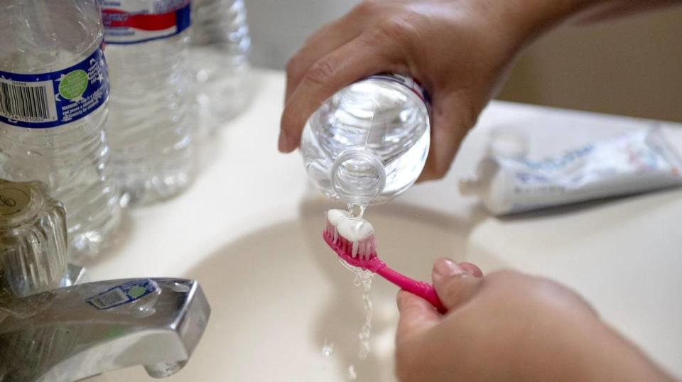 Jessica Martinez uses bottled water to brush her teeth on Friday, May 26, 2023, in Kansas City. Due to an outstanding balance left by a previous tenant, KC Water shut off water to Martinez’s home in April. Since then, the family has had to get creative for their water needs including transporting trash cans full of water by car to their home and using bottled water to brush their teeth.