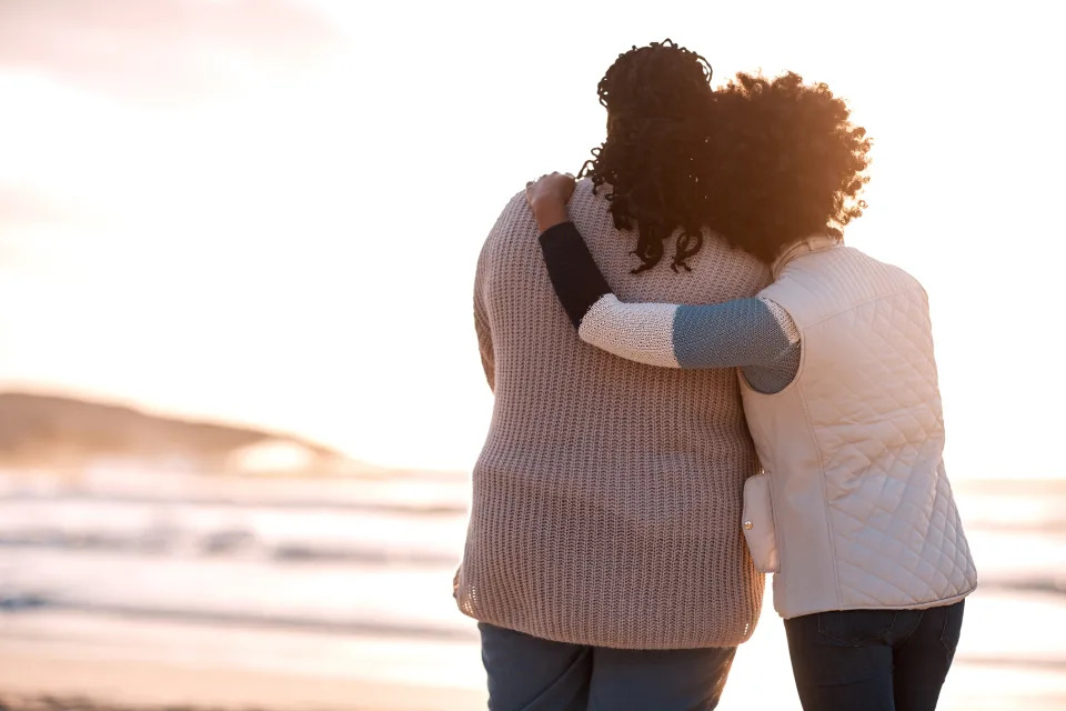 Two women hugging and looking out on a beach