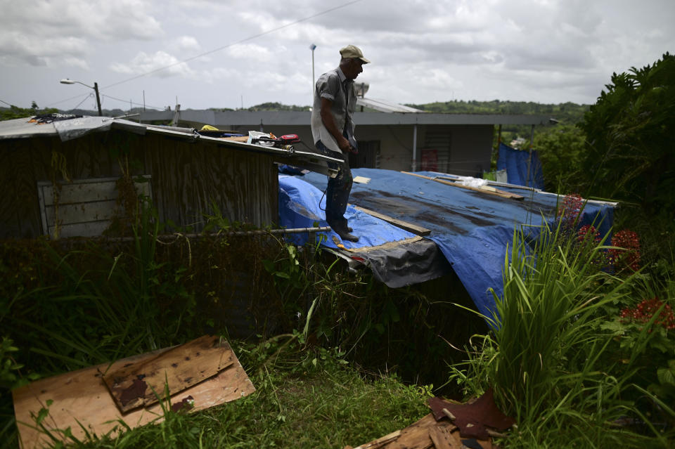 Wilfredo Negron stands on the rooftop of one of his properties securing the zinc roof in preparation for the current hurricane season, in Corozal, Puerto Rico, Monday, July 13, 2020. Nearly three years after Hurricane Maria tore through Puerto Rico, tens of thousands of homes remain badly damaged, many people face a new hurricane season under fading blue tarp roofs and the latest program to solve the housing crisis hasn't yet finished a single home. (AP Photo/Carlos Giusti)