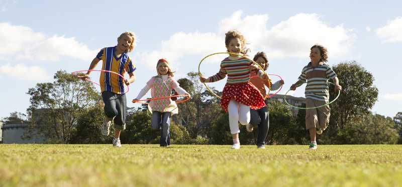 Children hoola-hooping together in a grassy field.