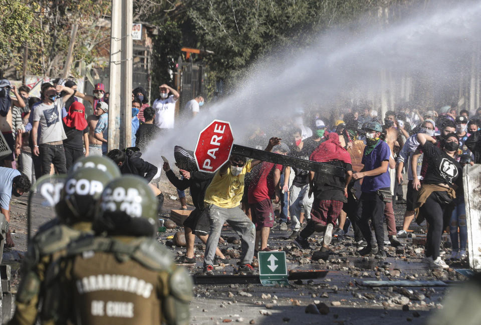 Manifestantes, algunos de ellos con mascarillas para protegerse del coronavirus, se enfrentan con la policía el lunes 18 de mayo de 2020 durante una protesta para exigir ayuda alimentaria del gobierno, en un vecindario pobre de Santiago, Chile. (AP Foto/Esteban Félix)