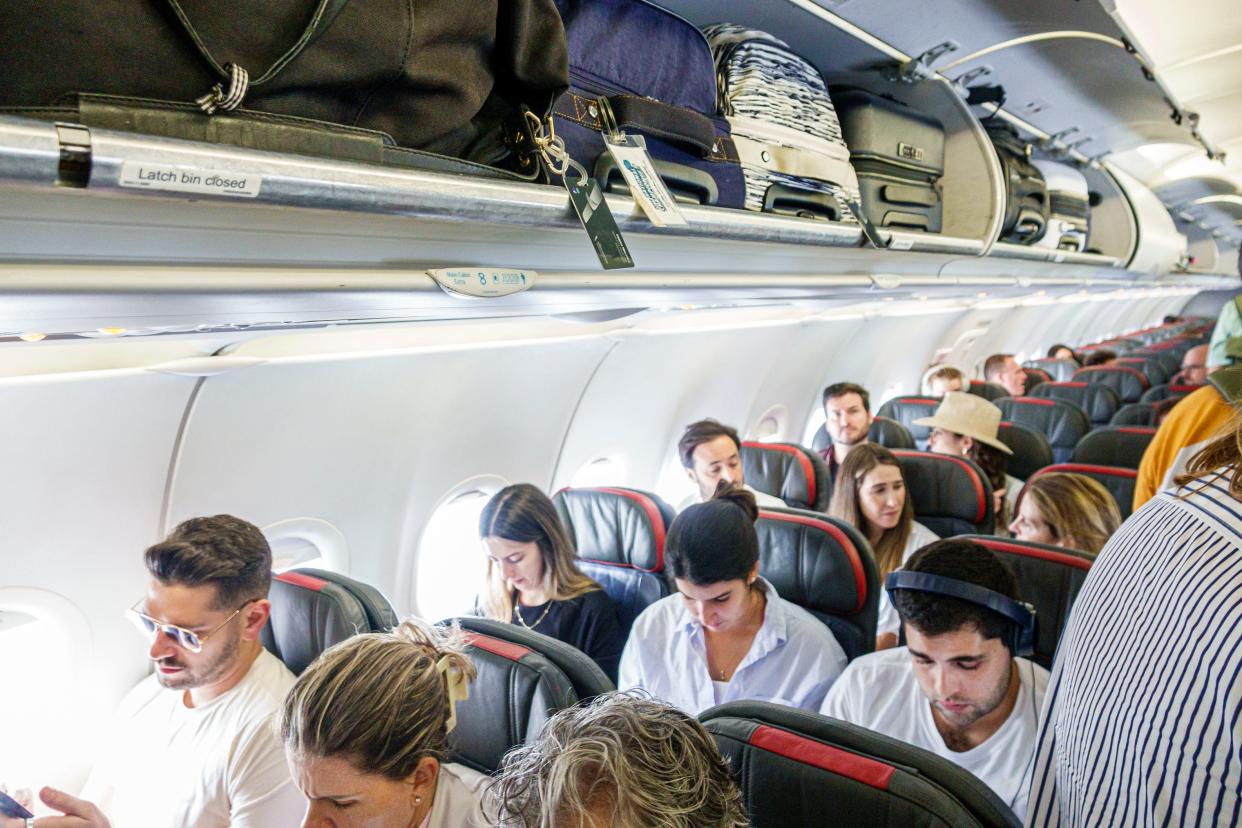 Passengers sat on a 3-3 narrowbody plane with overhead luggage bins open