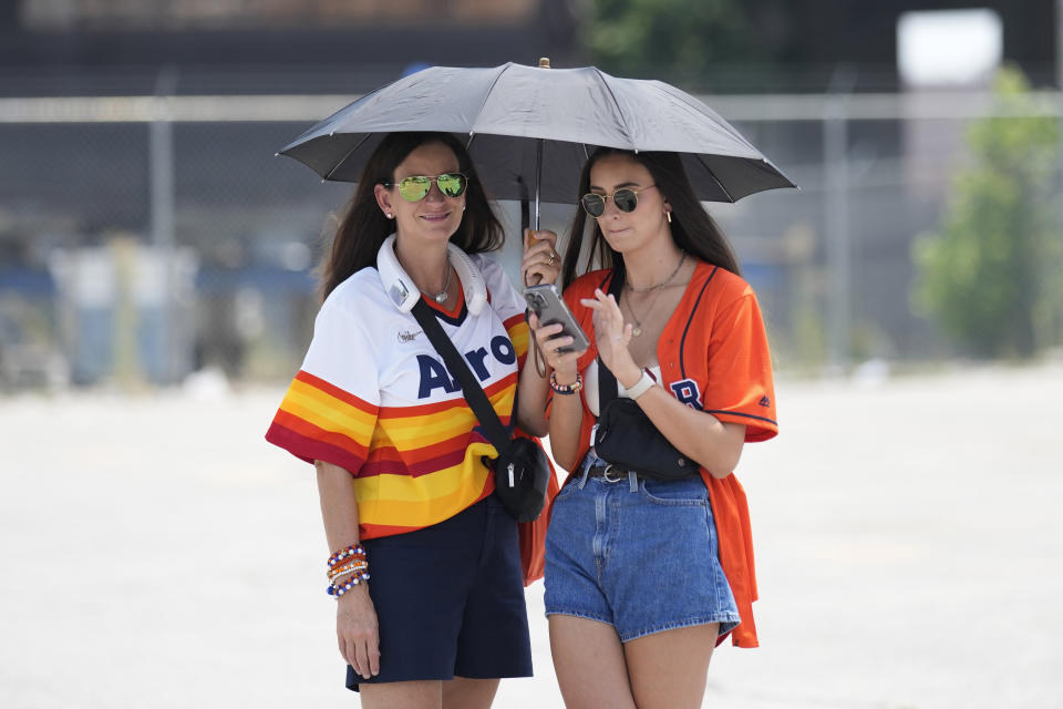 Kari Kile, left, wears a neck fan as she holds an umbrella over her daughter, Taylor, as they wait outside in the heat to enter Minute Maid Park for baseball game between the Cincinnati Reds and Houston Astros Saturday, June 17, 2023, in Houston. (AP Photo/David J. Phillip)