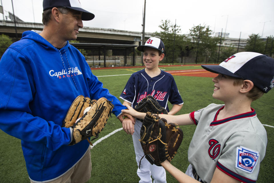 David Fox, from left, with his sons Dewey and Jimmy put their hands together as they wrap up practicing baseball at a nearby baseball field in northeast Washington, Friday, Aug. 23, 2019. David Fox and his wife, Mary Ann, have a rule for their sons, 11-year-old Dewey and 8-year-old Jimmy: They have to play a team sport. The kids get to choose which one. Dewey tried soccer and Jimmy had a go at flag football, but every spring and fall, their first choice is baseball. (AP Photo/Manuel Balce Ceneta)