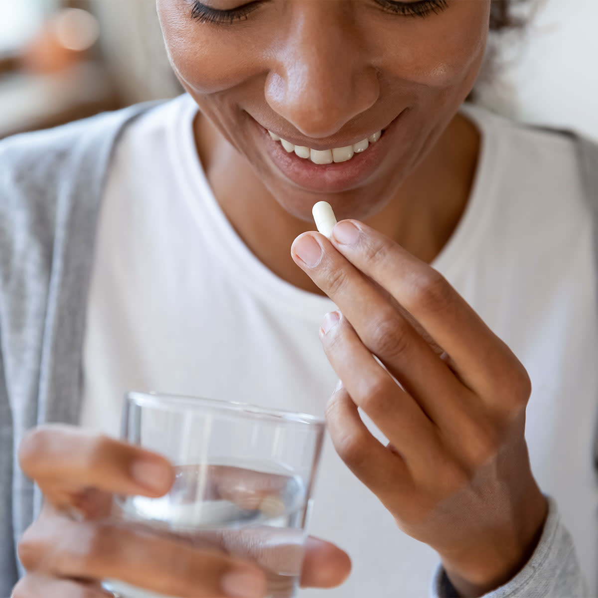 woman holding glass of water and taking probiotic supplement
