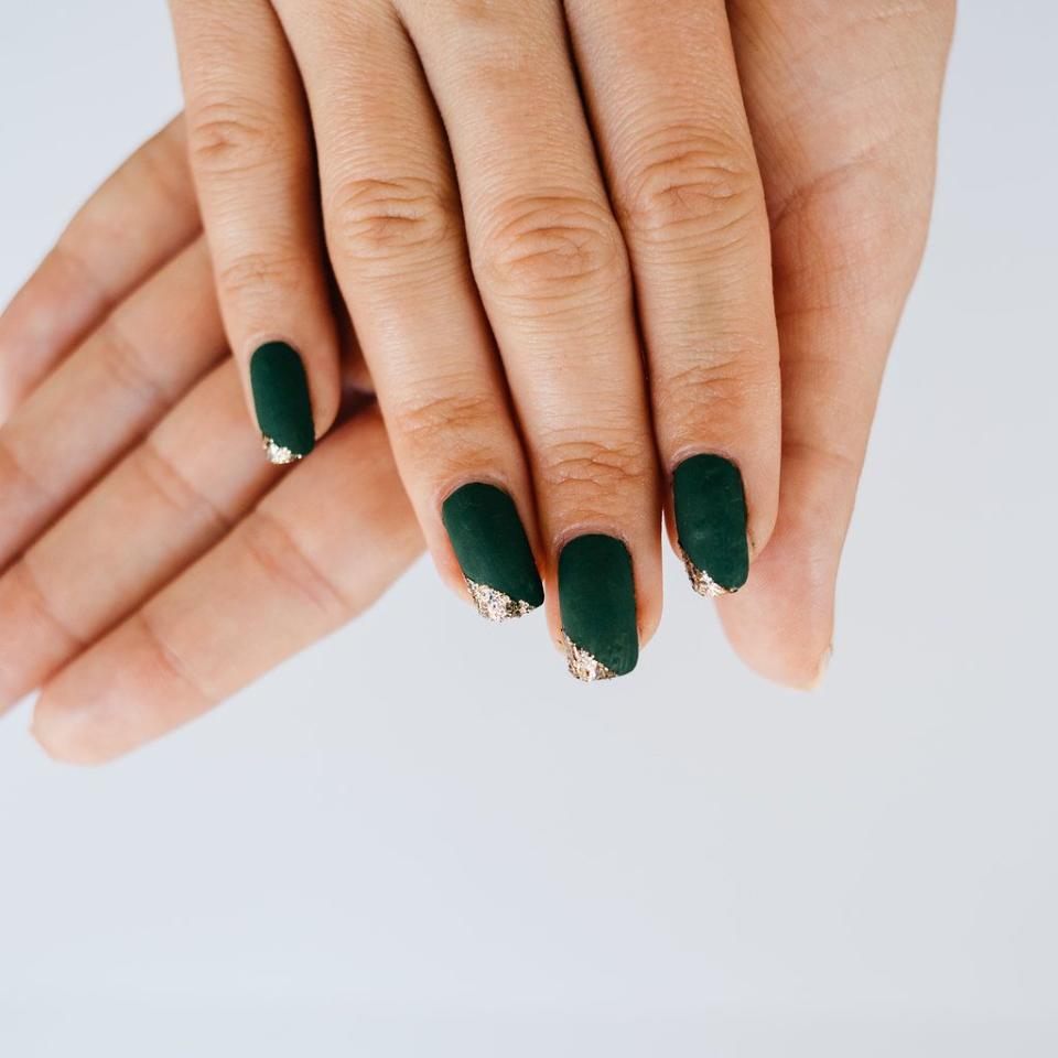 a hand with painted fingernails in dark green with an angled gold glittery tip on the nails