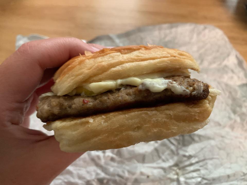 Hand holding Wendy's sausage, egg, and cheese croissant in front of white wrapper