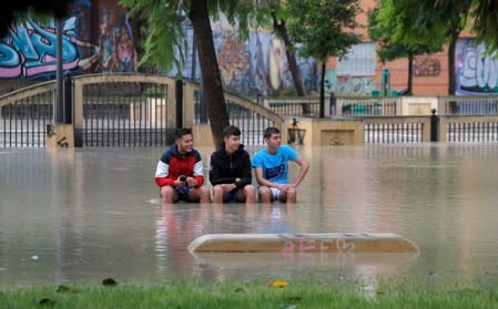 Boys sit on a bench in a park near the overflowing Segura river as torrential rains hit Orihuela