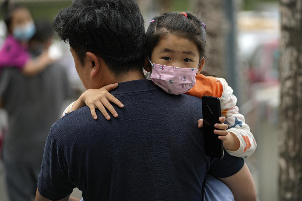 People carry their child wearing face masks to help curb the spread of the coronavirus head to a kindergarten in Beijing, Wednesday, June 9, 2021. (AP Photo/Andy Wong)