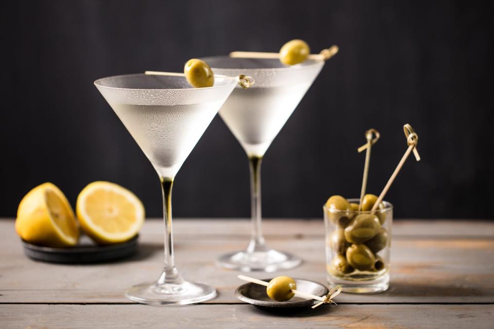 2 glasses of martini served with olives and lemon on a rustic grey worktop