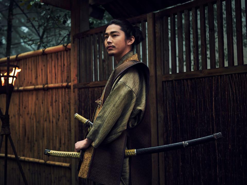 yuki kura as yoshii nagakado, a young main with two katana strapped to his waist and with black hair drawn back. he's wearing brown and green clothing