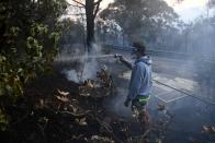 A resident hoses smouldering logs as a bushfire burns in Woodford NSW