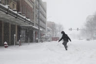 A pedestrian steps in tire tracks while crossing the street during a winter storm in downtown Lincoln, Neb. on Monday, Jan. 25, 2021. (Kenneth Ferriera/Lincoln Journal Star via AP)