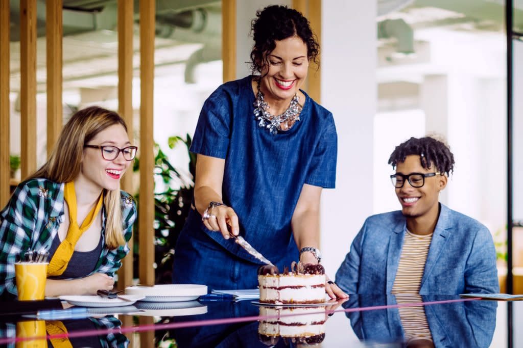 A woman cuts cake at the office. 